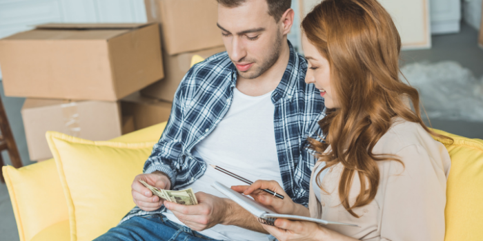 Couple sitting on the couch counting cash with boxes in background